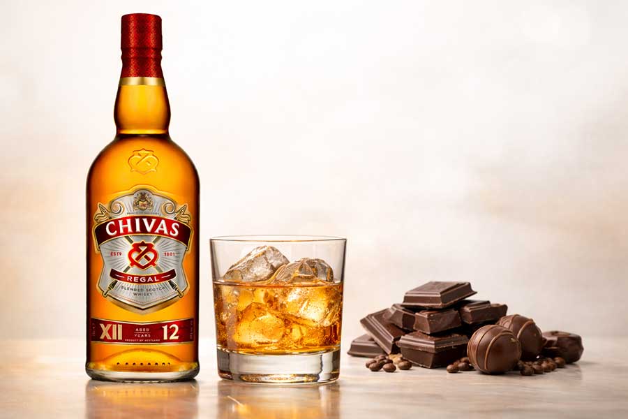 Botella de Chivas Regal 12 años, vaso de whisky con hielo y bombones de chocolate.